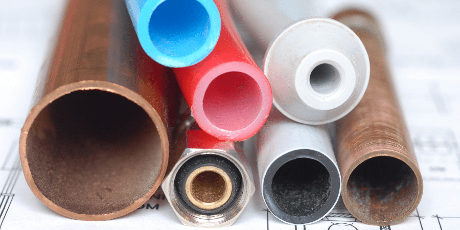 A close-up of various types of pipes, including copper, plastic, and metal, arranged on a blueprint.