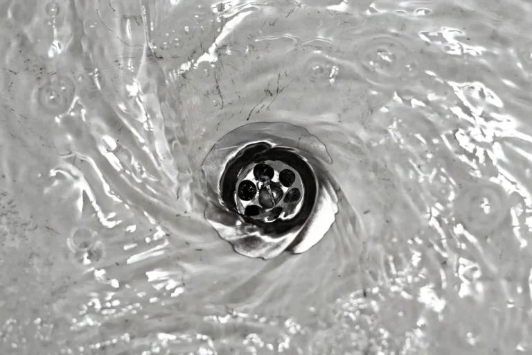 Water swirling down a metal drain, creating a vortex pattern.